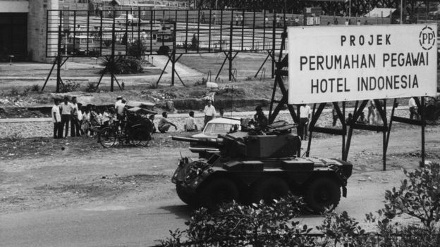 Young people stood outside an hotel in Indonesia with a military armoured vehicle on stand by